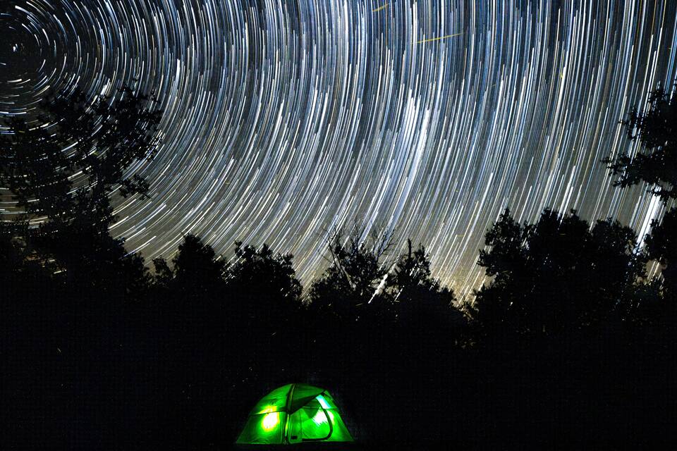 A star trail photograph with a green tent in the foreground.