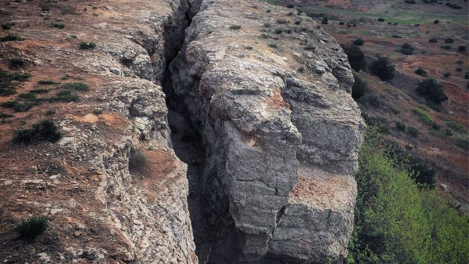A rugged cliff with a deep crevice, surrounded by sparse vegetation and a vast landscape.