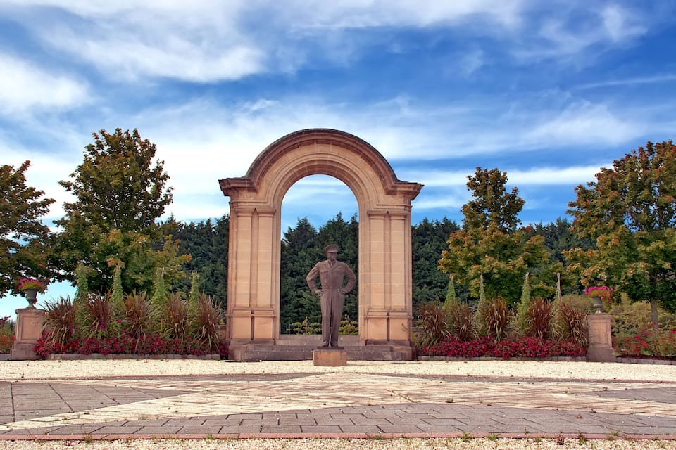A statue under an archway surrounded by landscaped gardens.