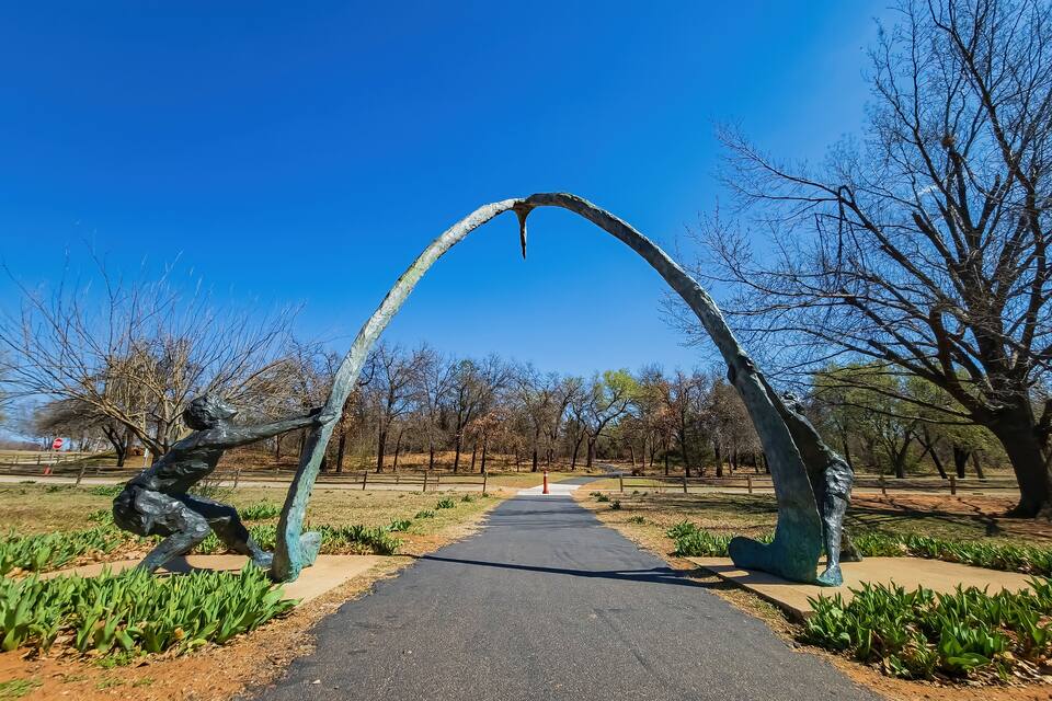 Un parque con un arco de escultura metálica y un sendero pavimentado.