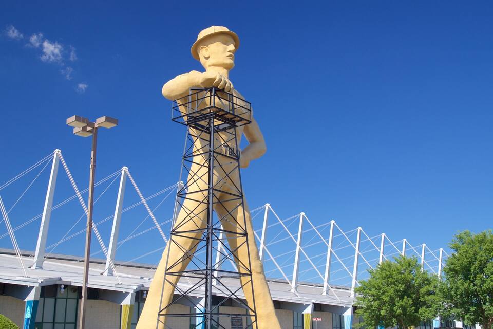 A large sculpture of a man in a hat, a tall tower, and a bridge with white cables.