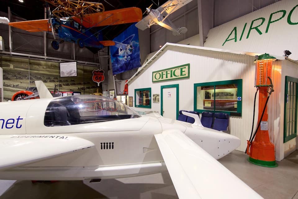 A small white airplane with 'romet' and 'experimental' written on it, an orange fire hydrant, and a building labeled 'AIRPORT OFFICE'.