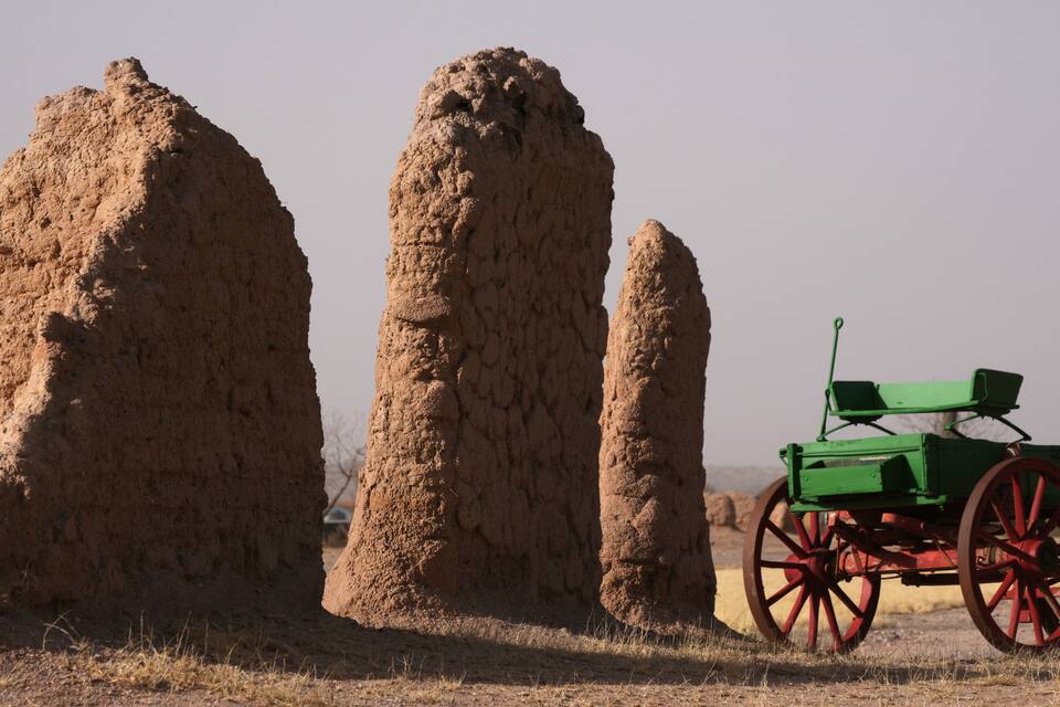 A green cart with red wheels in a dry, rocky landscape with large mounds of earth.