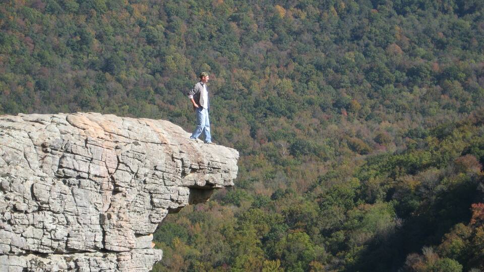 A person standing on a rocky cliff edge overlooking a forested valley.