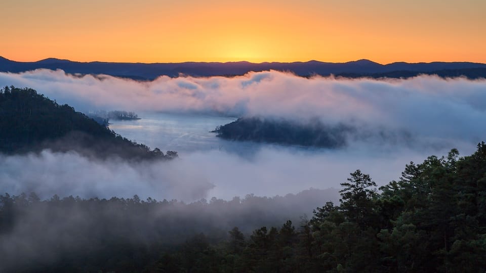 A sunrise over a valley with mist-covered hills and a river.