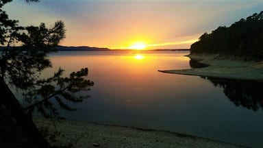 A sunset over a calm lake with a sandy beach and trees in the foreground.