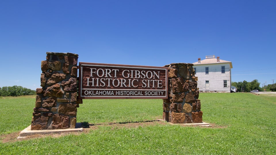 A sign for Fort Gibson Historic Site with a stone structure and a white building in the background.