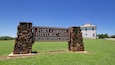 A sign for Fort Gibson Historic Site with a stone structure and a white building in the background.