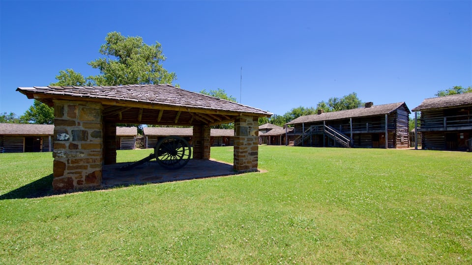 A historical site with a stone pavilion, wooden buildings, and a large cannon.