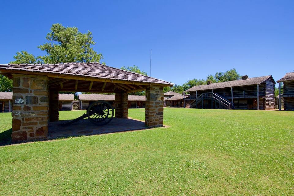 A historical site with a stone pavilion, wooden buildings, and a large cannon.