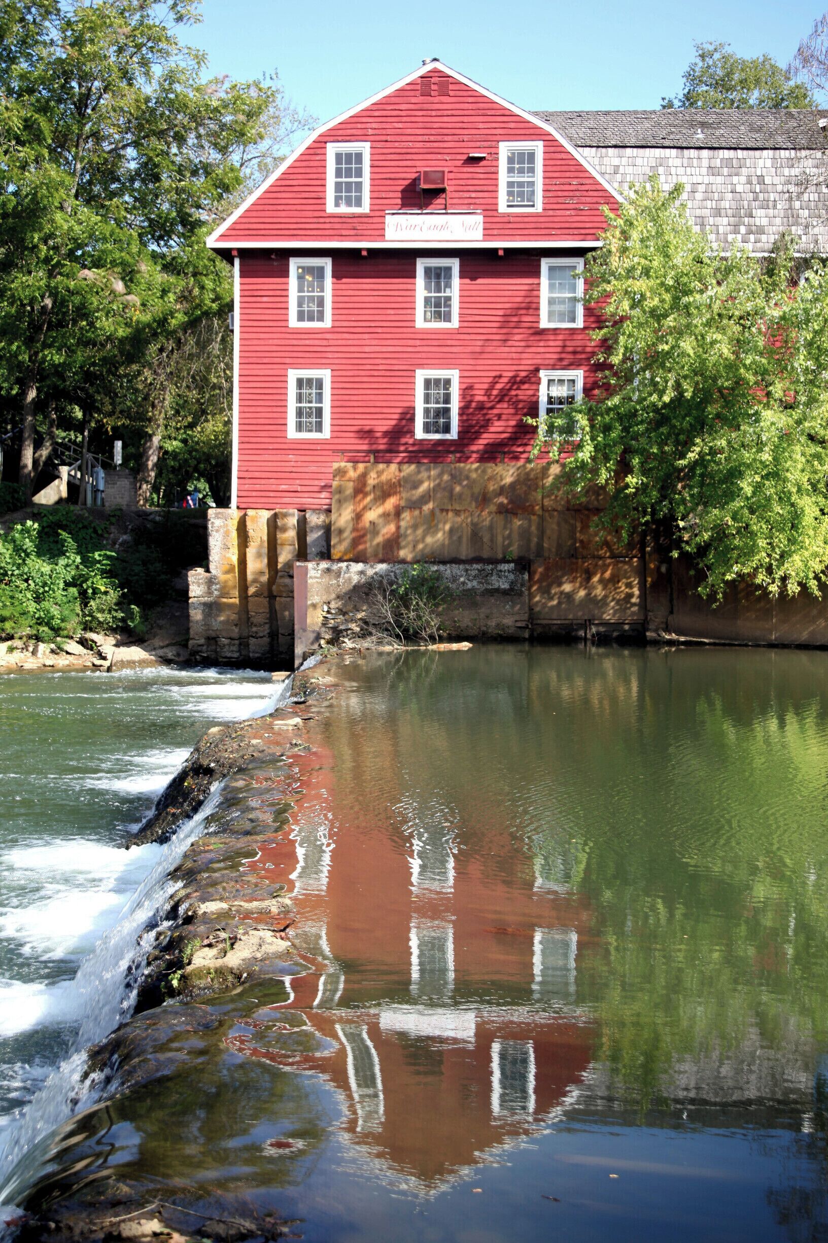 A red building with white trim, a river, and a tree in the foreground.
