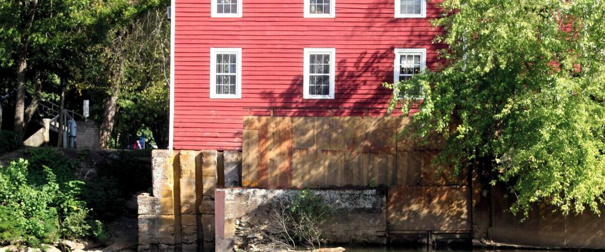 A red building with white trim, a river, and a tree in the foreground.
