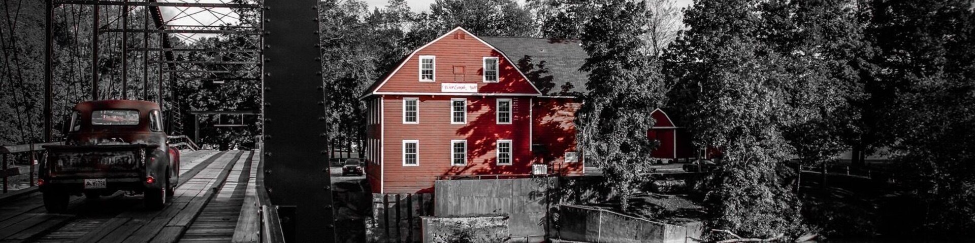 Un edificio rojo con un letrero que dice "The Old Mill", un puente de madera y un río.