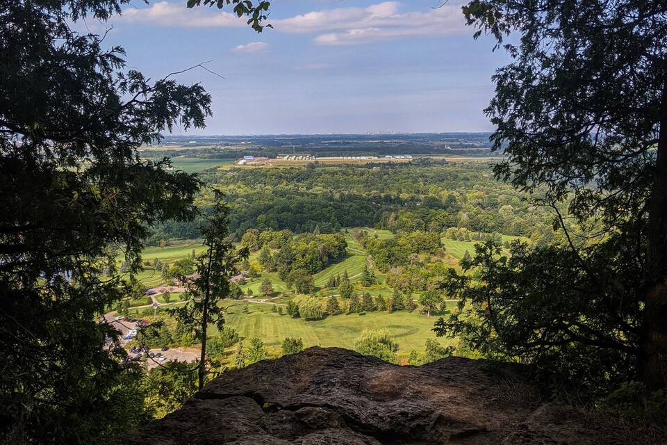 Un paysage boisé offrant une vue sur une vallée et des bâtiments situés au loin.