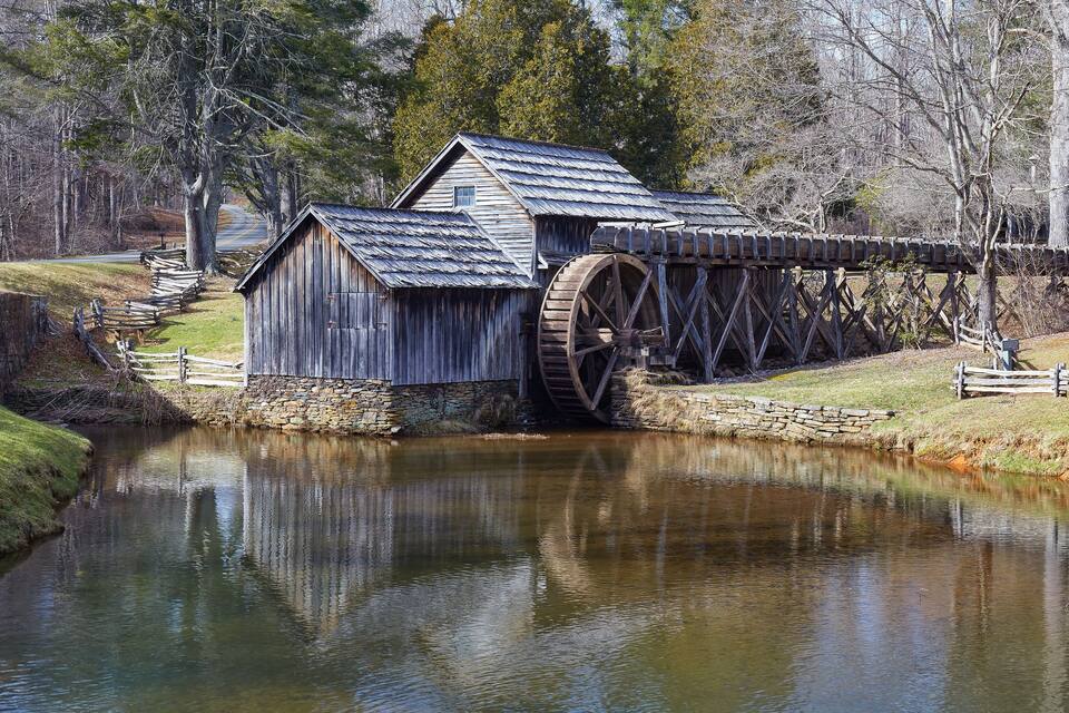 A wooden mill with a large water wheel by a calm river.
