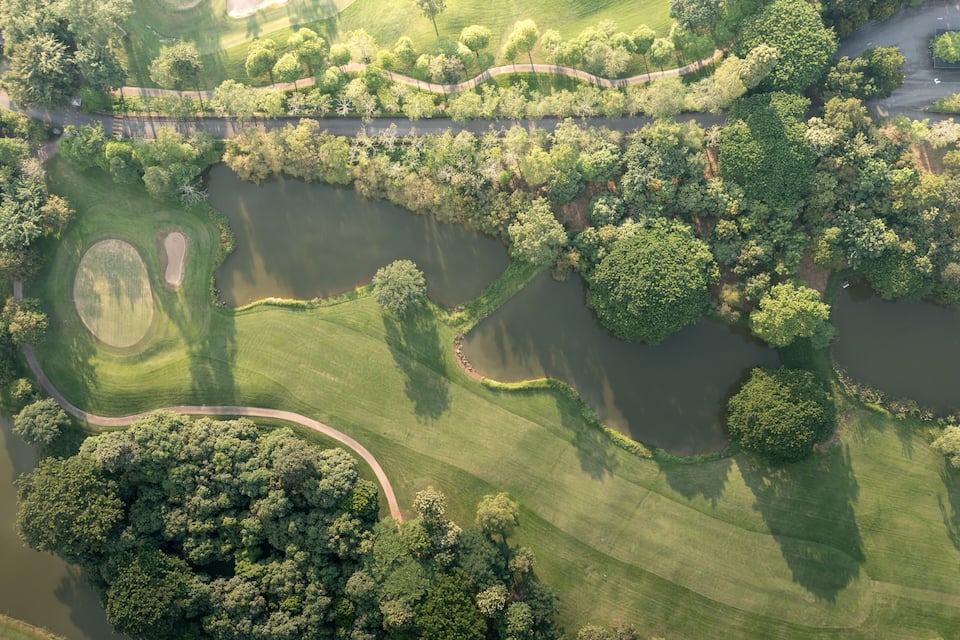 An aerial view of a golf course with a pond, surrounded by lush greenery and trees.