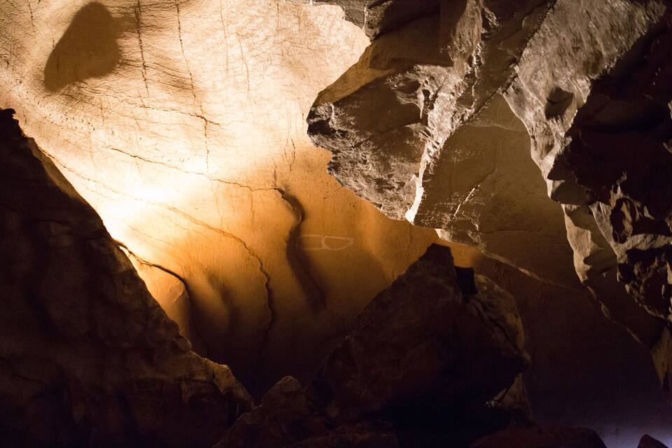 A cave interior with rock formations and a light source illuminating the cave floor.
