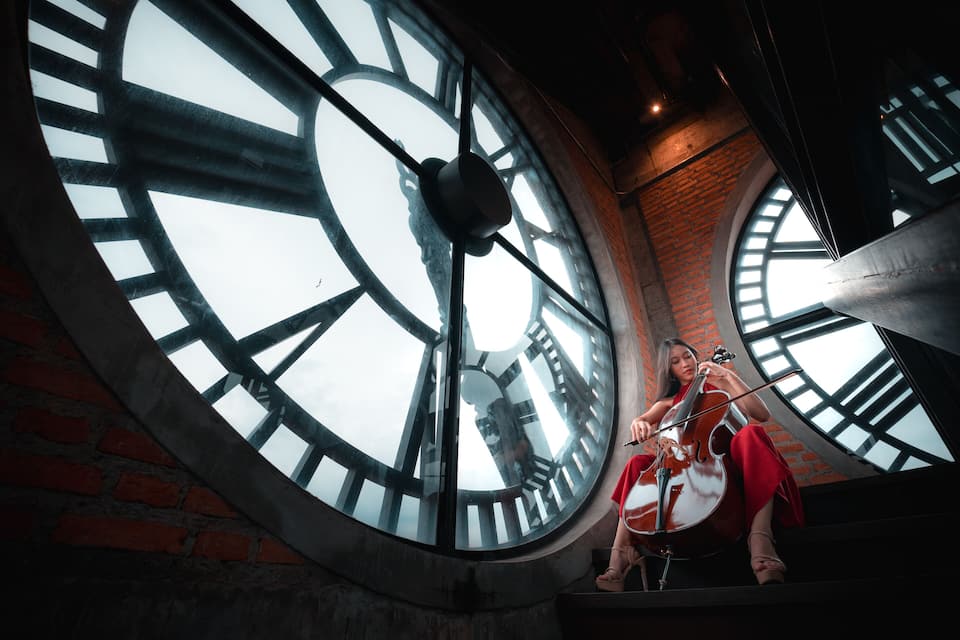 A person playing the cello in front of a large circular clock.