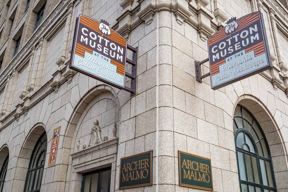 The exterior of the Cotton Museum at the Memphis Cotton Exchange, featuring large signs and the Archer Malmo building.