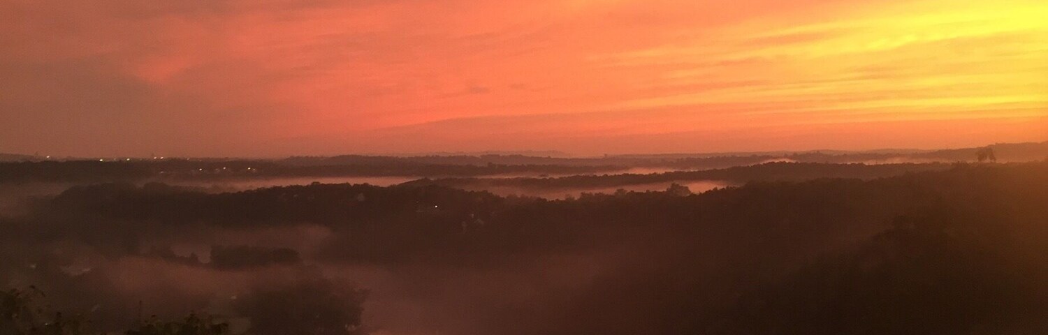 Um pôr do sol sobre um rio, com vegetação ao redor.