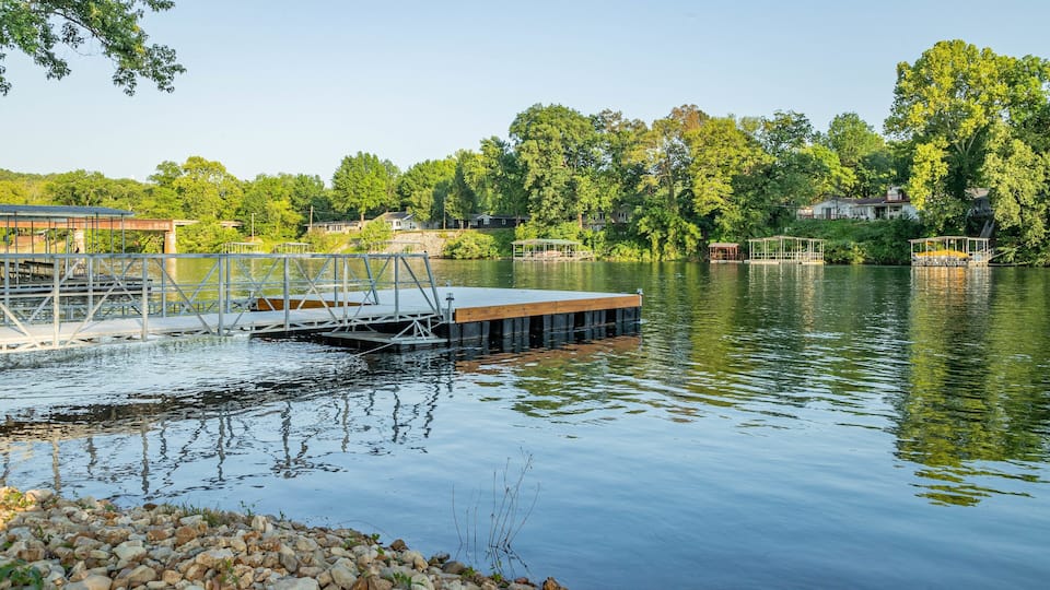 A calm lake with a dock, surrounded by lush greenery and residential buildings.