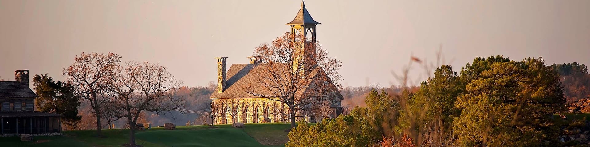 Stone chapel on a hill surrounded by autumn foliage at sunset
