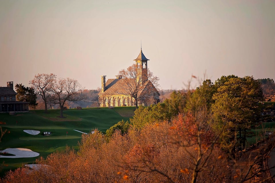 A church with a steeple, surrounded by autumn trees and a golf course.