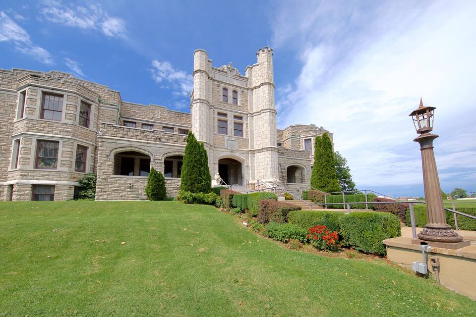 A large stone building with a tower, surrounded by well-maintained lawns and trees.