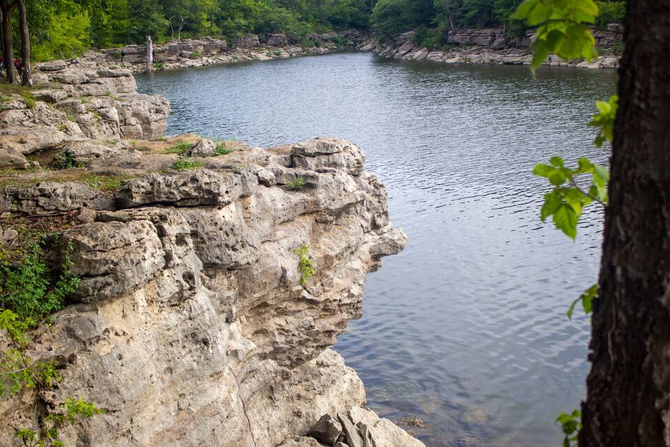 A rocky cliff overlooking a calm river with dense greenery in the background.