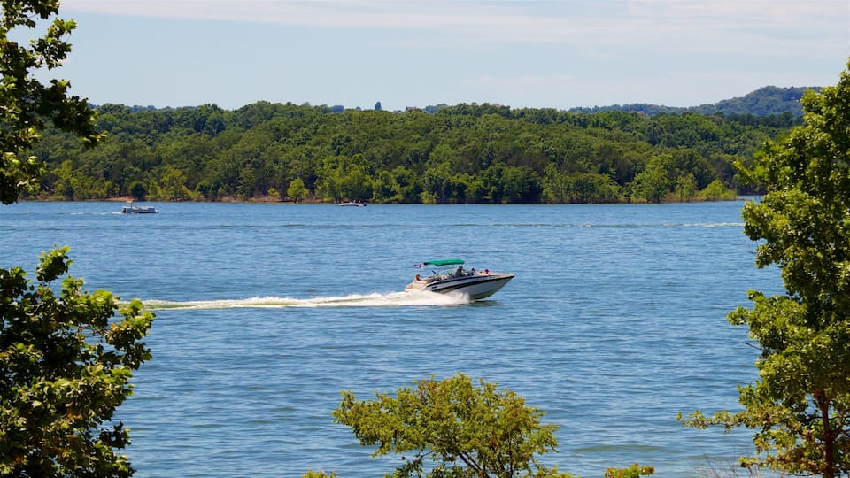 A boat speeding across a calm lake surrounded by dense green forest and hills in the background.