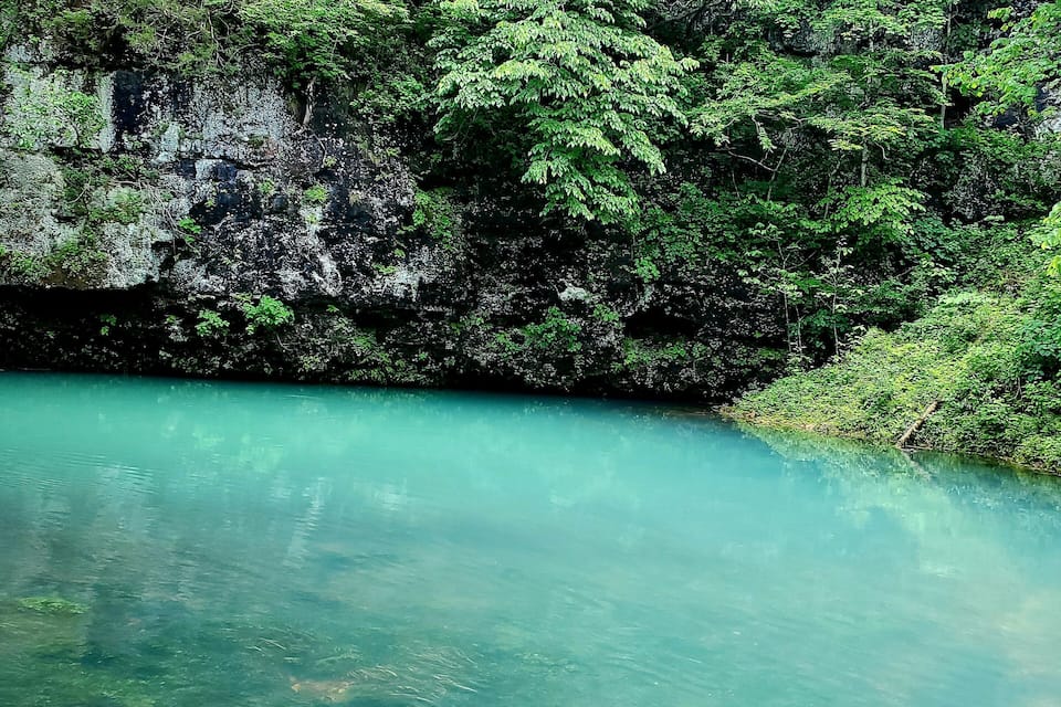 Een helder turquoise rivier omgeven door weelderige groene begroeiing en rotsachtige kliffen.