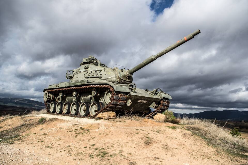 A military tank on a dirt path with mountains in the background.