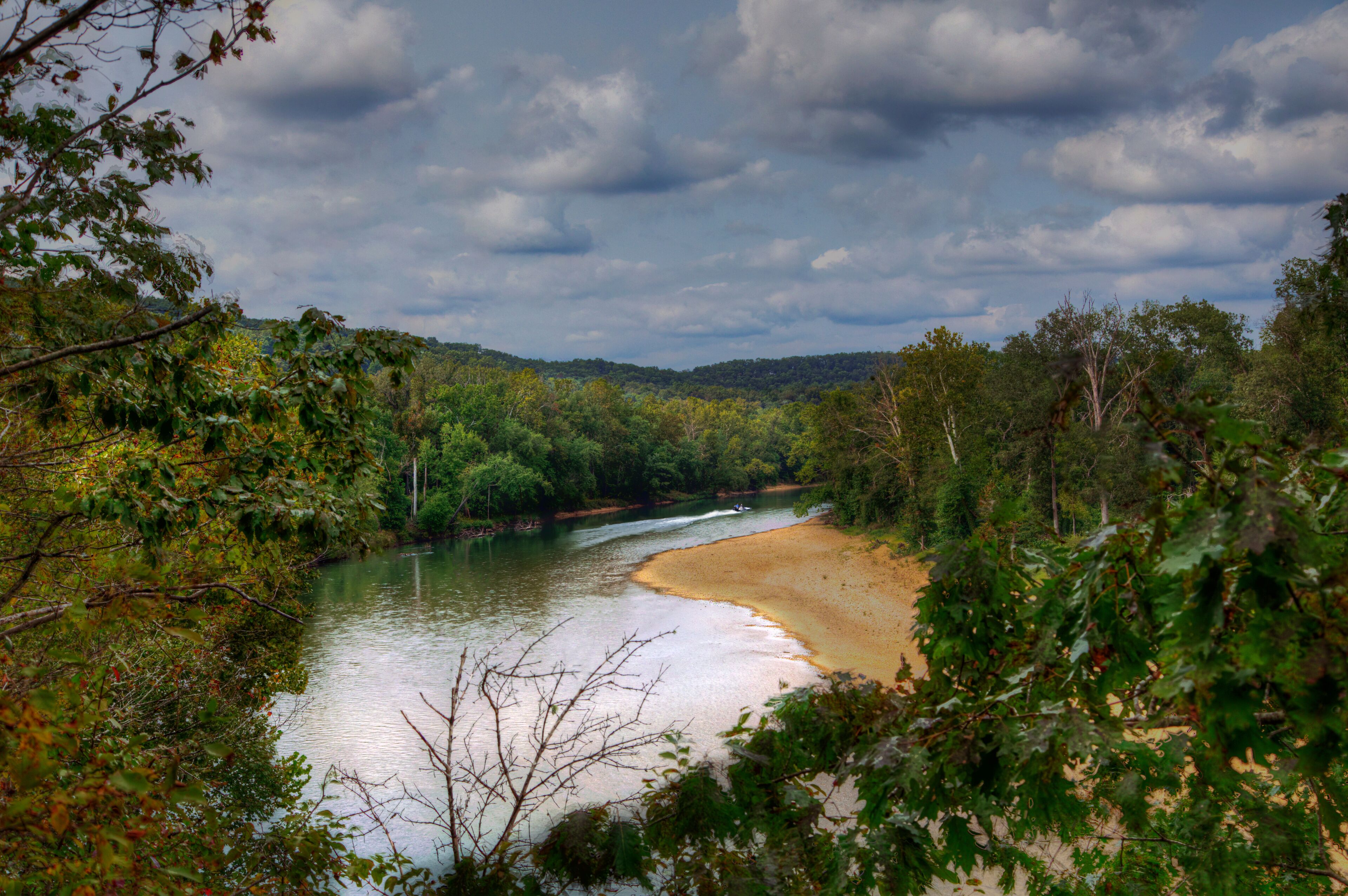 A river flowing through a forested area with a sandy beach.