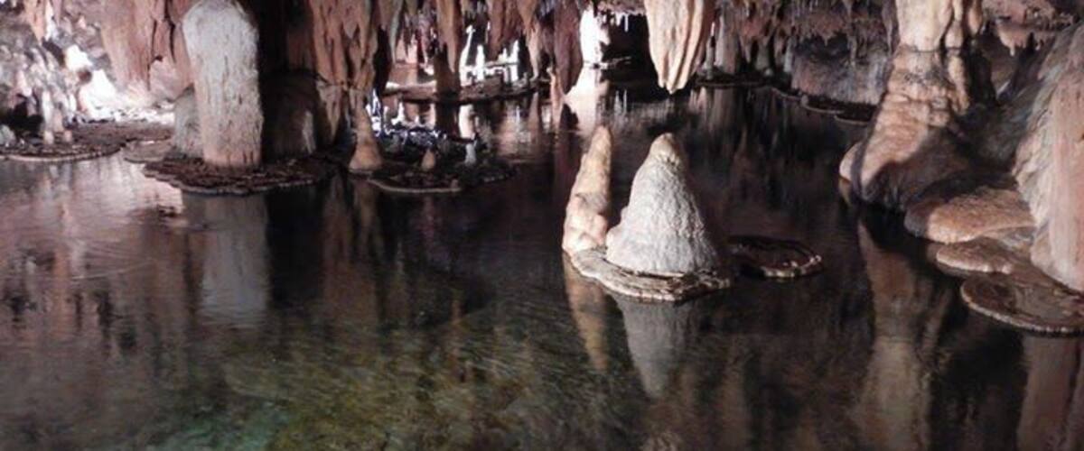 A cave with stalactites, stalagmites, and a reflective water surface.