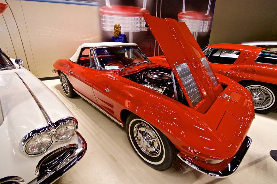 A red vintage car with its hood open, displaying its engine.
