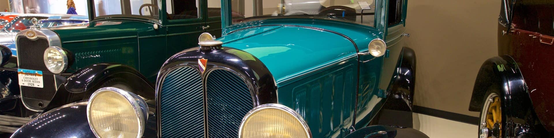 A vintage car with a teal body and black accents, including round headlights and a prominent grille.