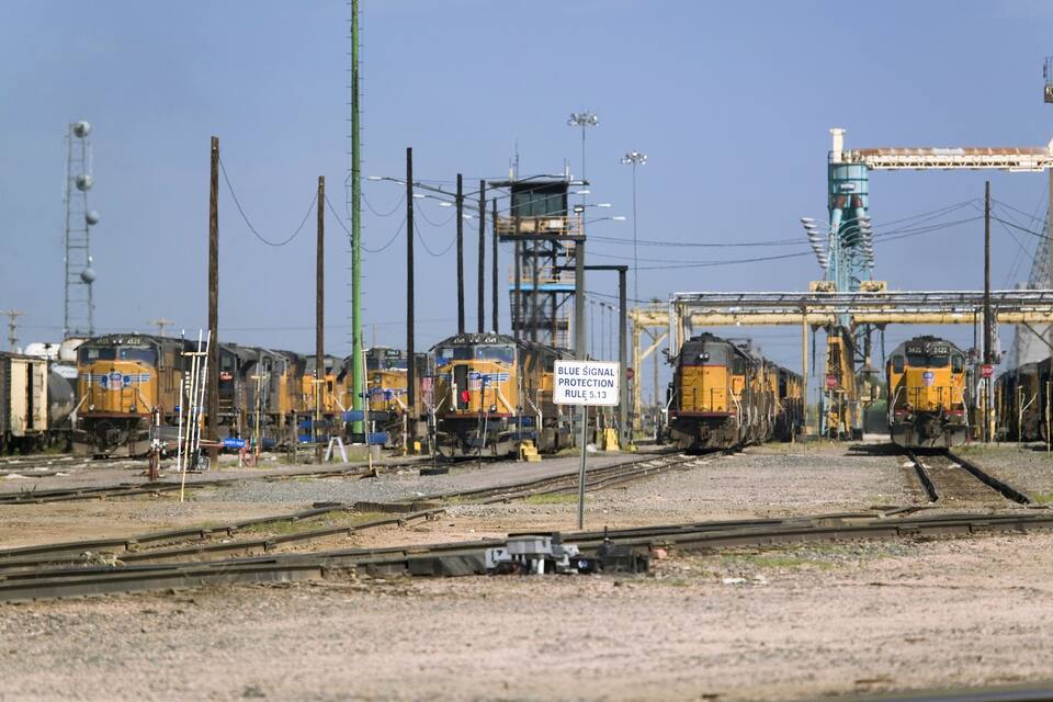 Une cour de triage ferroviaire avec plusieurs trains et un panneau bleu indiquant les règles de sécurité des signaux.
