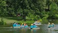 People riding small boats on a calm river surrounded by lush greenery.
