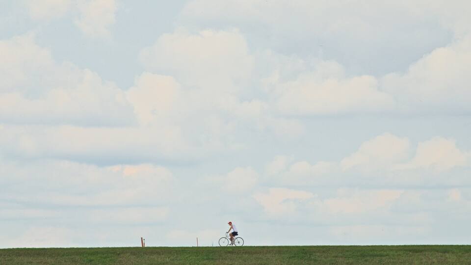 A cyclist riding on a grassy field with a cloudy sky.