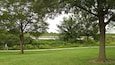 A park with a walking path, trees, and a body of water in the background.