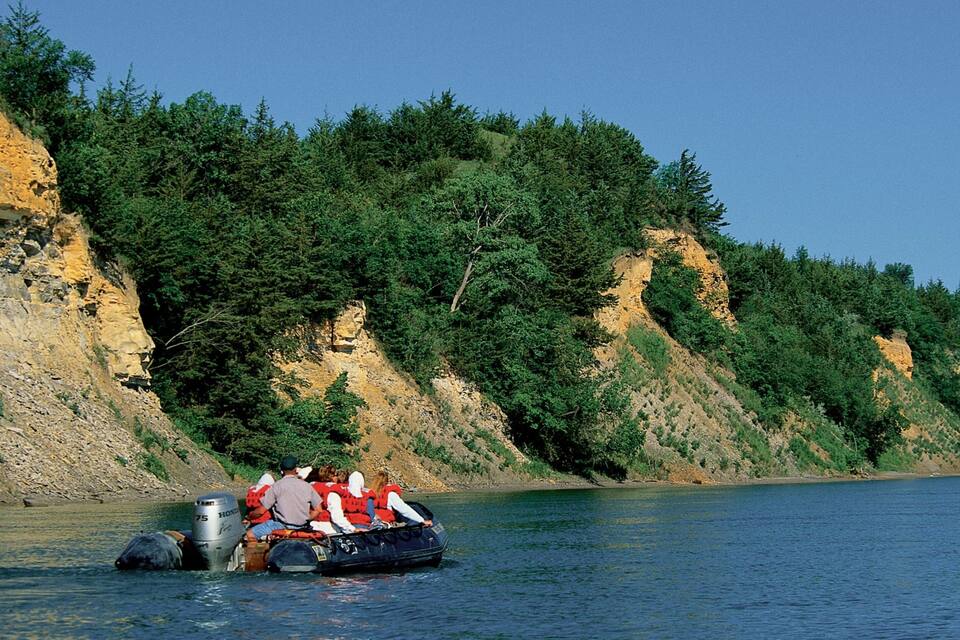 A group of people in a boat on a river with cliffs and dense forest in the background.