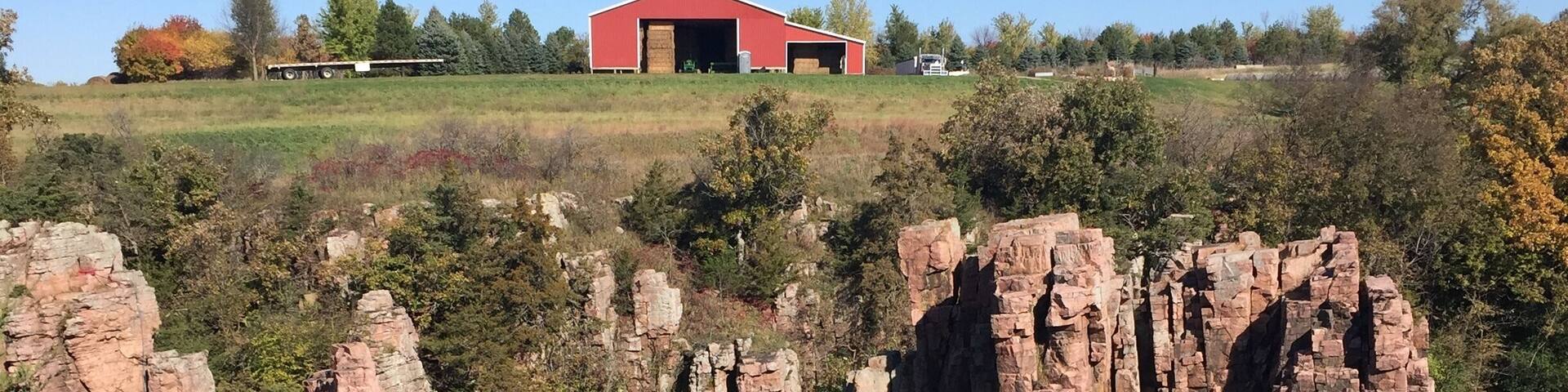 A red barn on a hill, rocky cliffs, and a river.