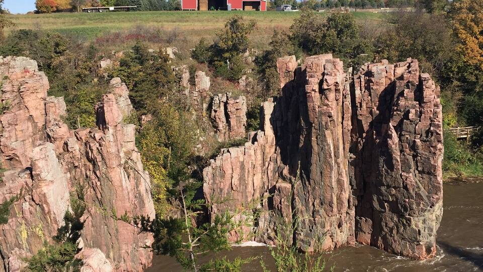 A red barn on a hill, rocky cliffs, and a river.