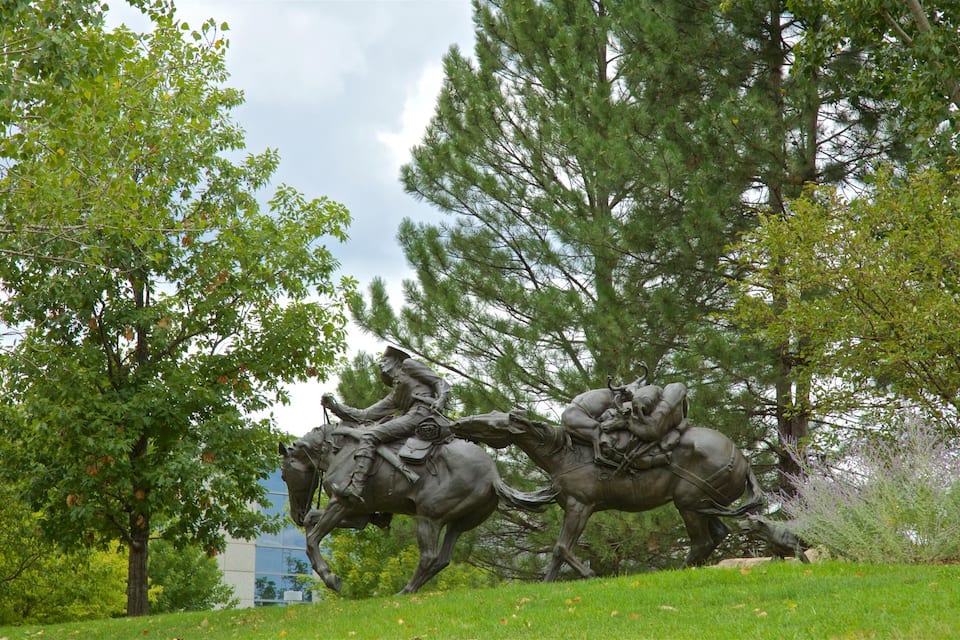 A bronze equestrian statue in a park with trees and grass.