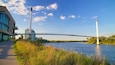 Een kabelbrug over een rivier, met moderne gebouwen aan de linkerkant en weelderige begroeiing aan de rechterkant.