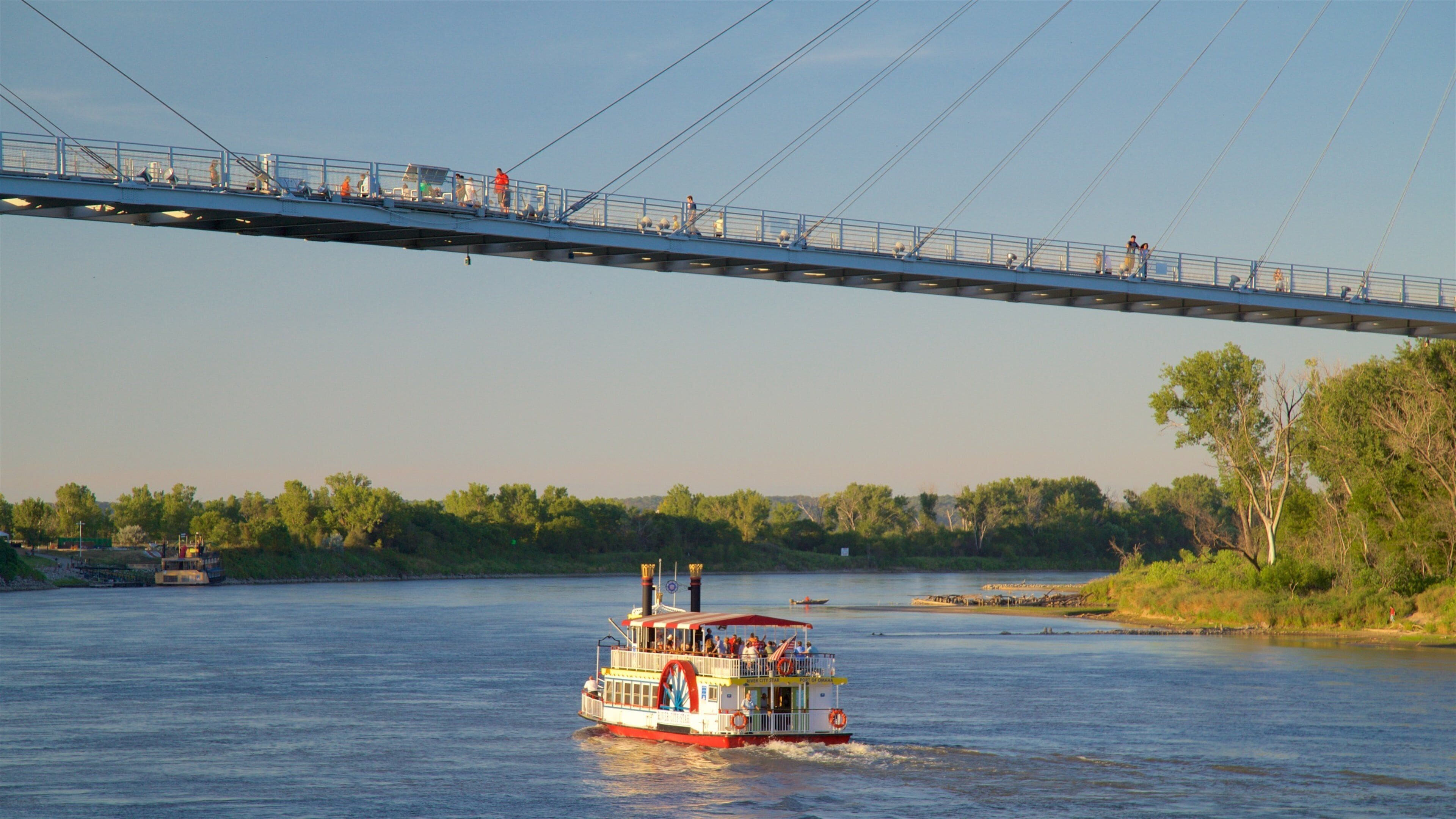A riverboat on a river with a bridge overhead.