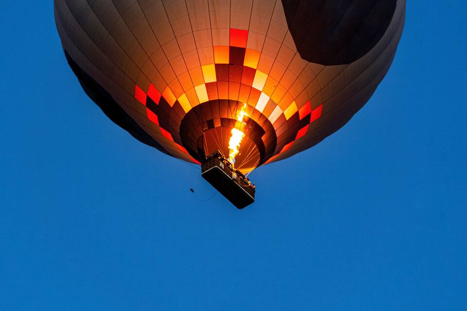 Um balão de ar quente com padrão vermelho e preto, subindo contra um céu azul límpido.