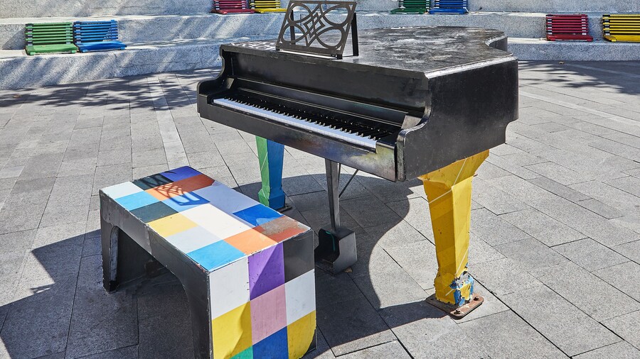 Black piano in the city square, colored benches around. Music concept