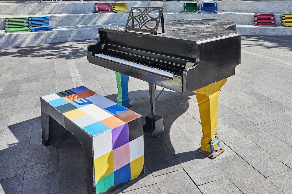 A black piano with a colorful stool in an outdoor setting.