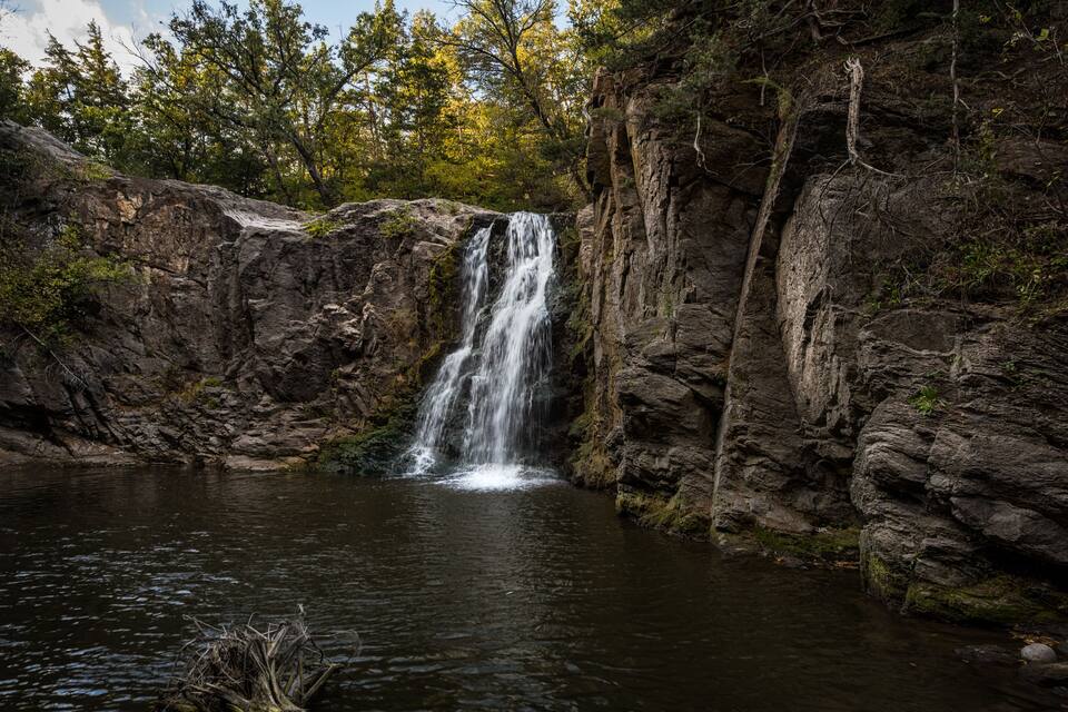 A waterfall cascading into a calm pool surrounded by rocky cliffs and trees.